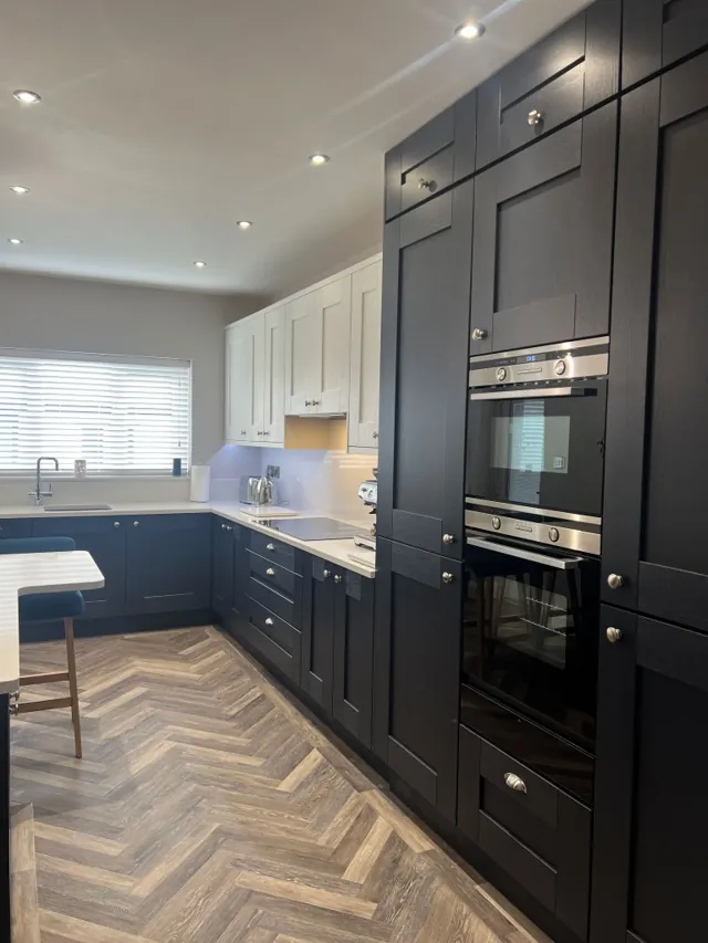 Dark Shaker kitchen with double ovens and herringbone floor in an open-plan room