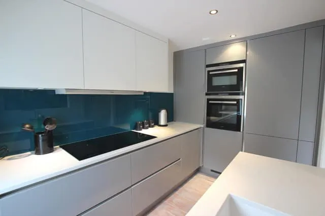 Handleless grey kitchen with teal glass splashback and white worktops