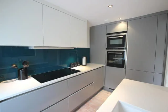 Handleless grey kitchen with teal glass splashback and white worktops