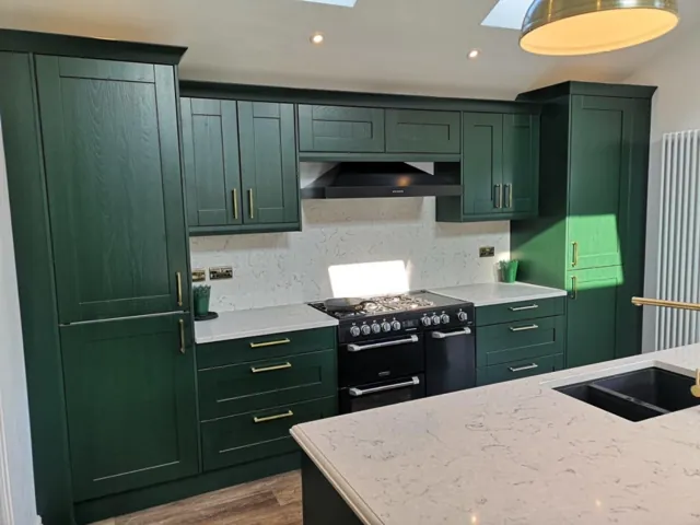 Green Shaker cabinetry with range cooker, brass handles and pale stone worktops