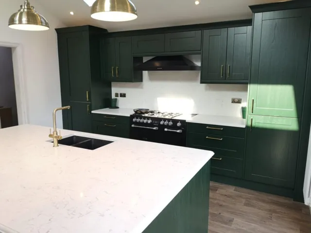 Green Shaker kitchen with brass pendant lighting and stone island with inset sink