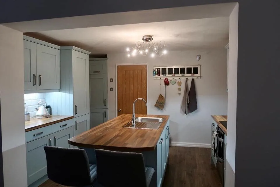 Sage green Shaker kitchen with curved timber island and breakfast seating