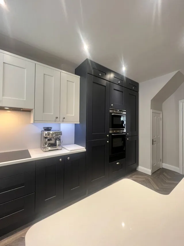 Black tower units with built-in ovens alongside cream cabinetry and white worktops